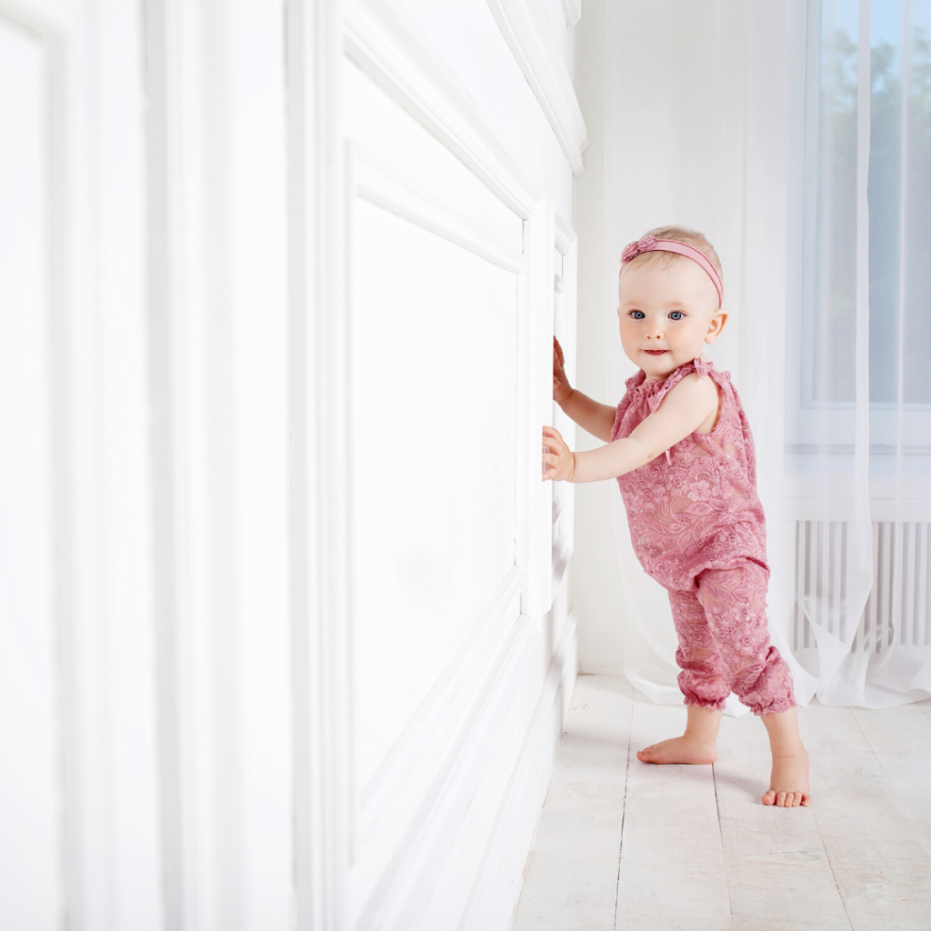 build the confidence to travel solo
baby girl, dressed in pick playsuit and headband taking her first steps, leaning against a white wall