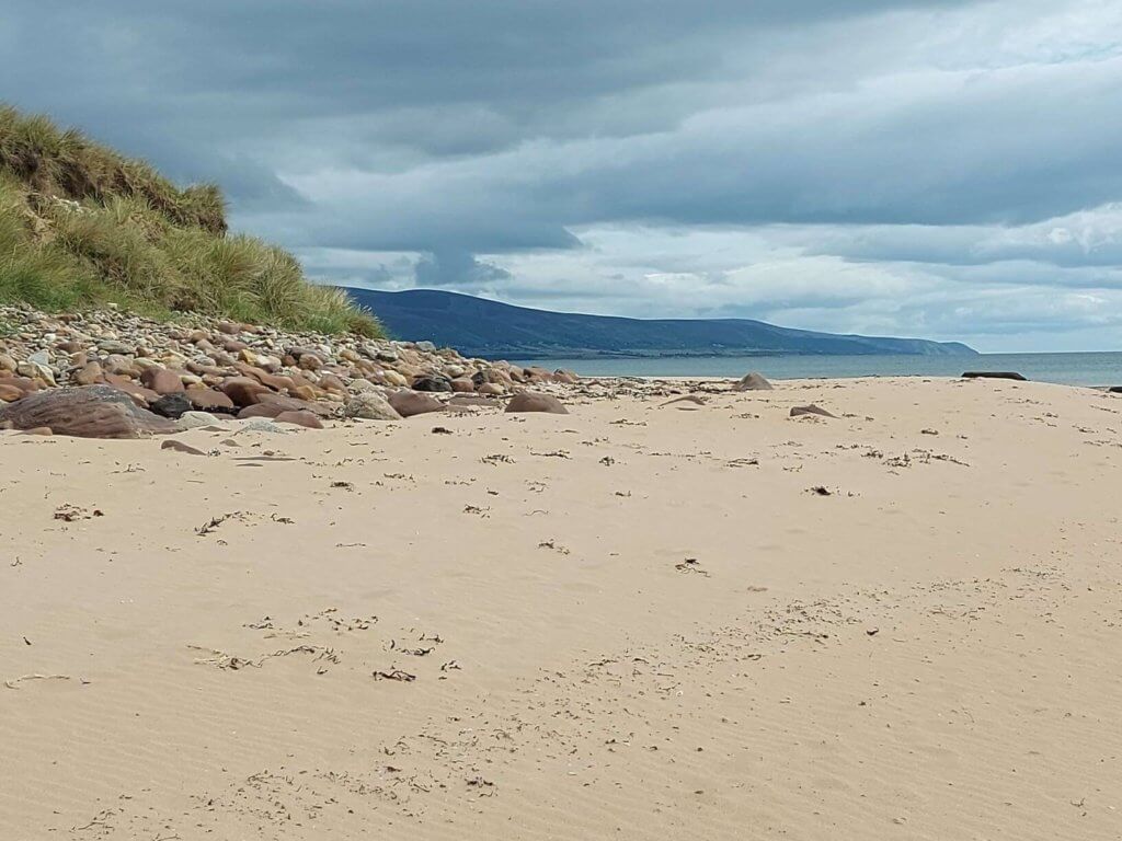 Solo female travel 
sandy beach with blue cloudy sky and grassy dunes to left