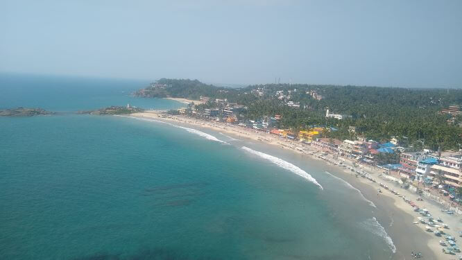 Drone shot of by with turquoise sea and strip of beach with town on edge