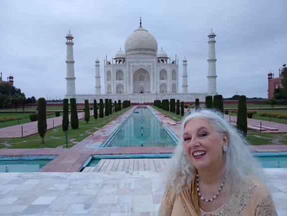 Solo female travel in India 
Older grey haired woman in from of Taj Mahal, White Marble temple with ponds running between the teo