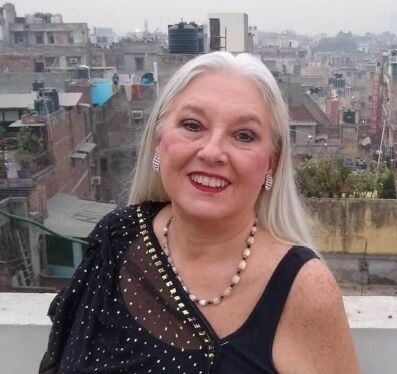 Solo female travel in India 
Older woman with long grey hair wearing black and gold sari scarf and vest top, cream necklace and red lipstick.  Background of many flats in city area