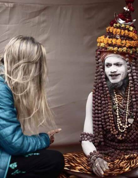 Solo female travel in India 
Woman with long blonde hair wearing blue jacket facing away from camera speaking with man covered in white body paint, wearing many brown beaded necklaces and headpiece