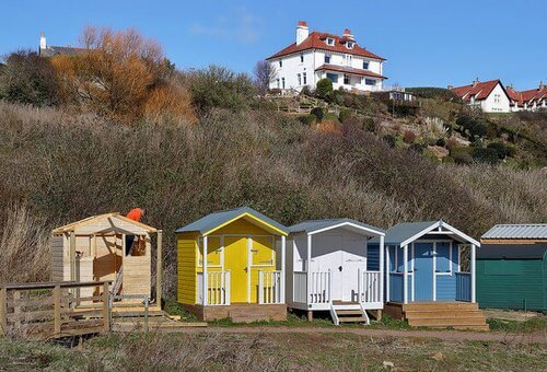 Day trips from Edinburgh colourful beach huts, yellow, white and blue set against cliff with white house at top and blue sky