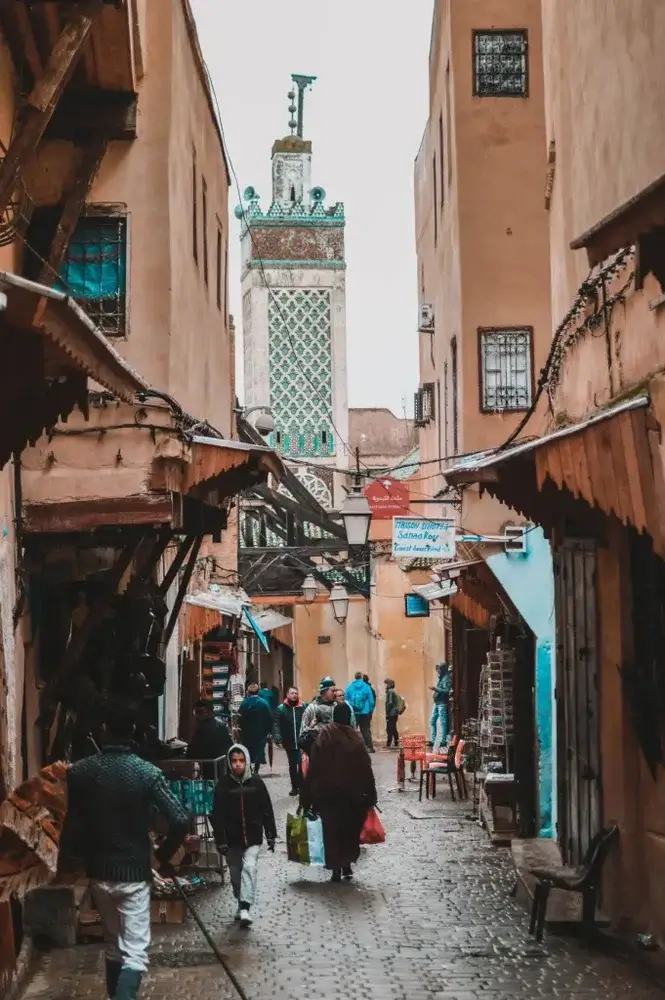 Second city Fez, Morocco.  A street in the medina with cobbles, locals and a ornate white and green tower in the background