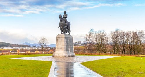 Day Trips from Edinburgh In search of history
Statue with stone base and bronze of horse and rider set in neat mown grass houses and trees in distance behind blue sky