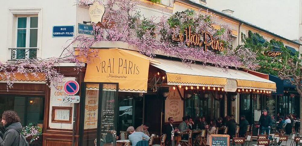 paris cafe with pink flowers over canopy and outside seating 