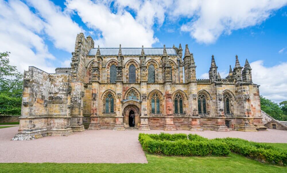 Roselyn Cahpel, stone built church with gothic arches and decorative stonework against a backdrop of blue sky with white fluffy clouds