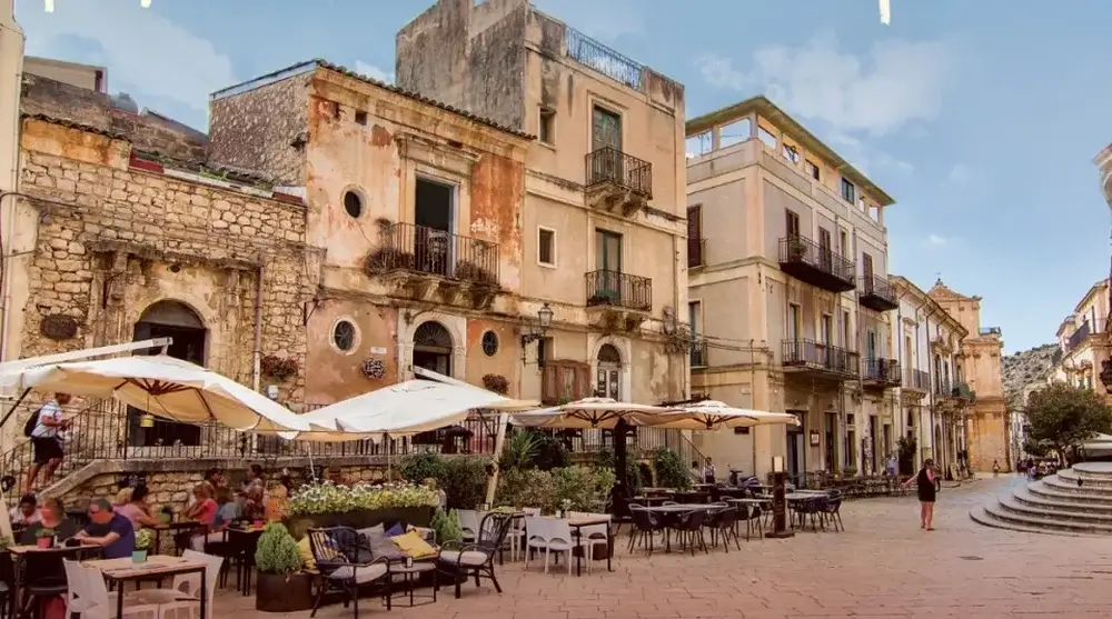 Being a tourist in Venice
Plaza or square.  Pinky creamy old buildings with iron balconies frame outside seating with large cream umbrellas and some people seated at left