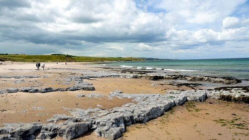 Yellow sandy beach with some rocks, people in distance and turquoise sea