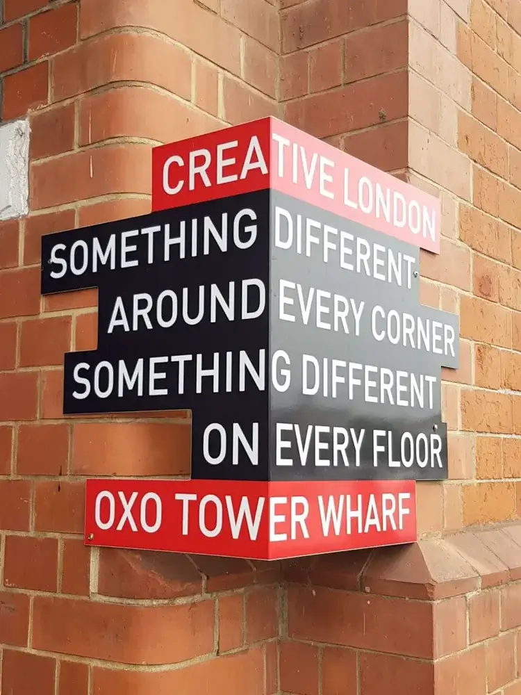 Sign on corner of building in black and red with white writing saying 'creative London something different around every corner something different on every floor oxo tower wharf