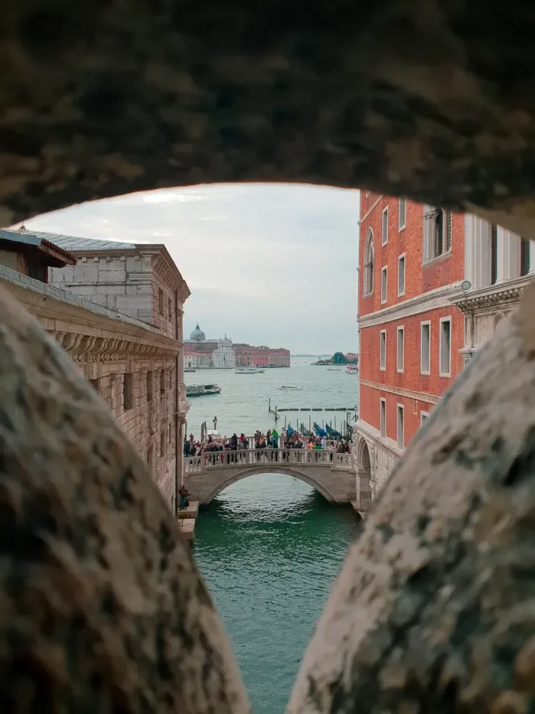 Looking out between stonework onto canal and bridge crowded with tourist