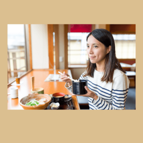 build the confidence to travel solo
Woman in blue and white stripey top eating with chopsticks, noodles from a bowl at a window seat in a cafe with orange table.