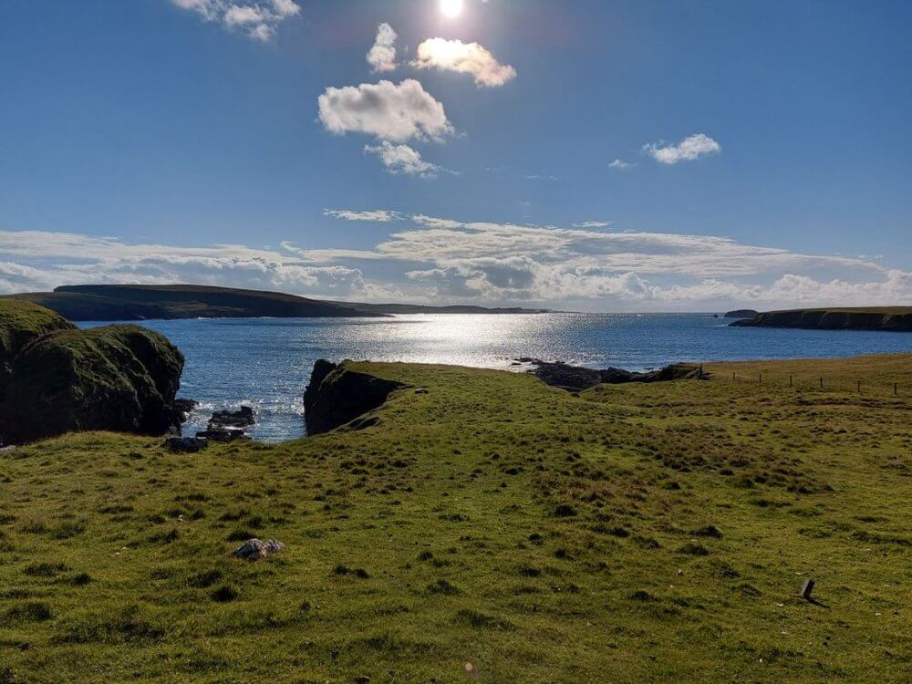 Road Trip Shetland
Grassy cliff top overlooking sea to distant cliffs with blue sky with a few white clouds