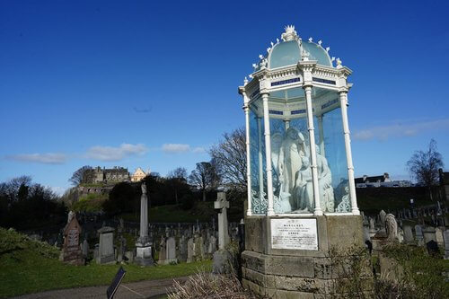 Day Trips from Edinburgh.  Image of Glass tomb with angel statue in white inside surrounded by many gravestones, blue sky