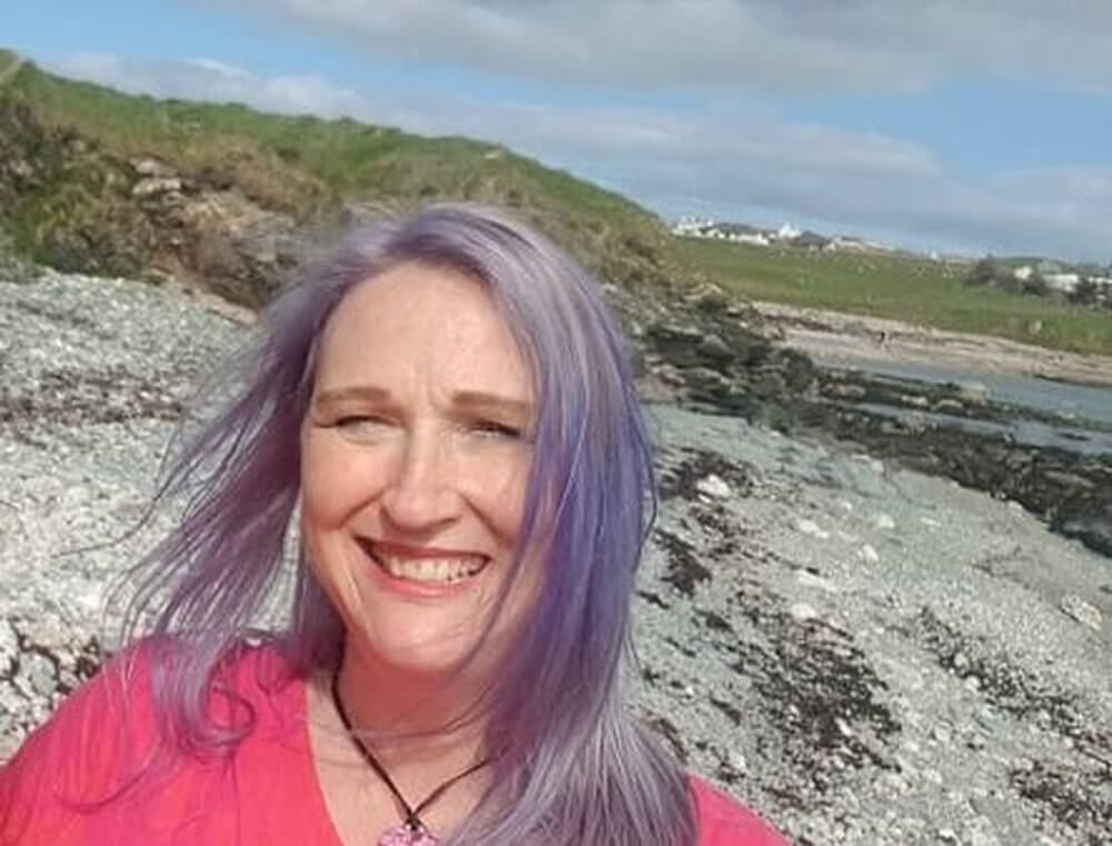 Woman with lilac hair in a bright pink dess standing on a pebble beach