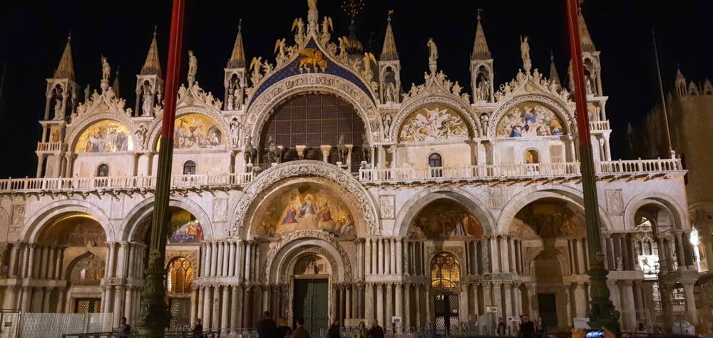 Front of St Mark's Basillica lit up at night.  Intricate carvings and paintings with decorative stonework