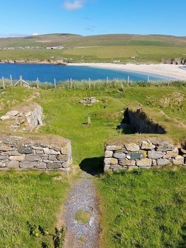 Ruin of a church overlooking sandy beach and blue sea, green fields in background, blue sky