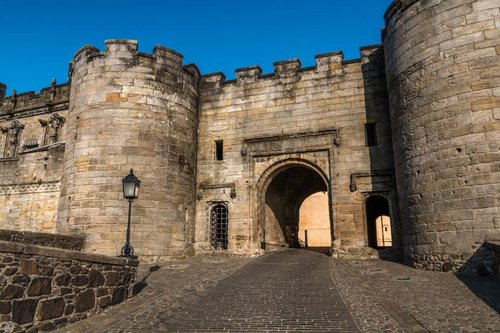 Grand arched entrance to castle with turrets and cobbled approach road