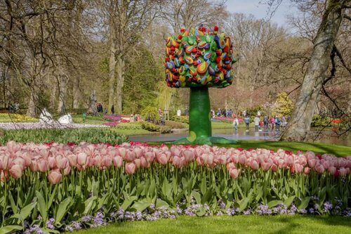 Keukenhof Art installation, green tree with multi coloured shapes, leaves and a gheko, pink tulips in front and trees in background