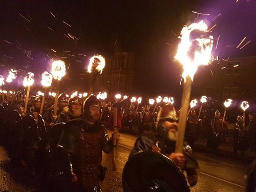 Men dressed as Vikings wearing helmets and carrying flaming torches in a processions