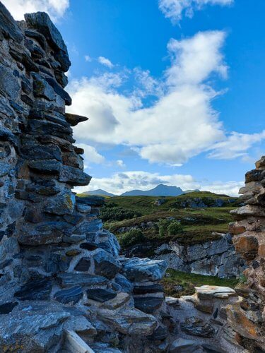 View from ruin of castle, stone wall, rolling green hills mountain in distance, blue sky with white fluffy clouds