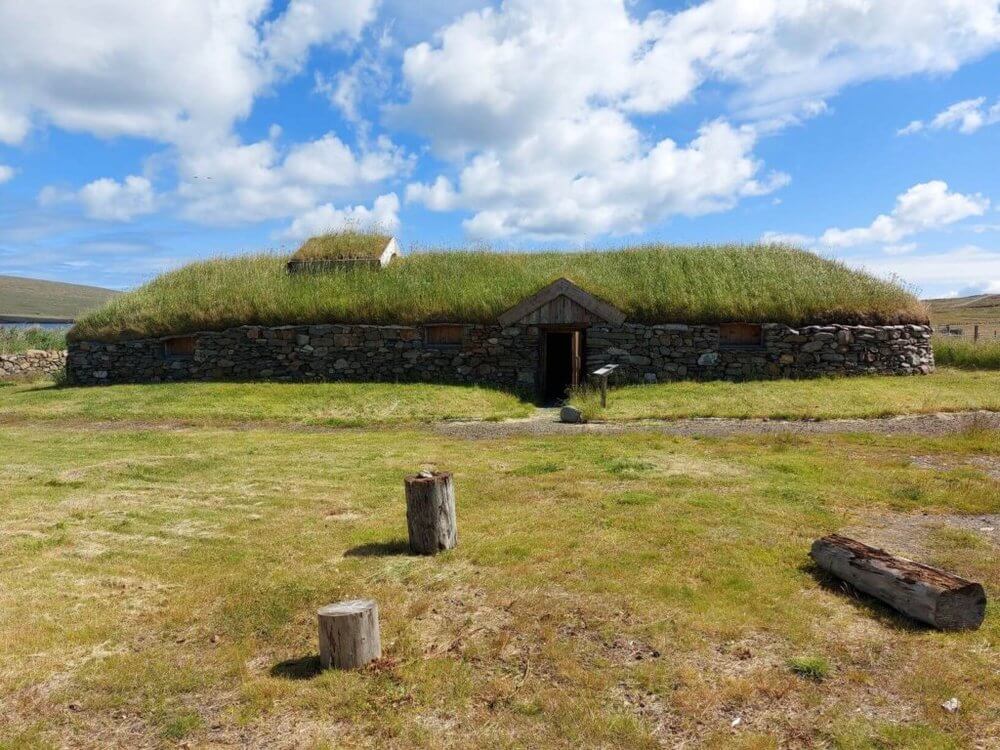 Road trip Shetland
Single story stone longhouse with grass roof, grass to foreground and blue sky with white clouds