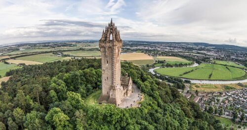 In search of history
Drone shot of stone tower surrounded by trees on top of hill, rive rand fields in distance below