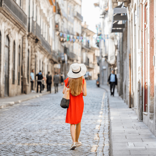 embracing solitude during solo travel as a woman over 40. Woman in a red dress and straw hat walking away from camera along cobbled street