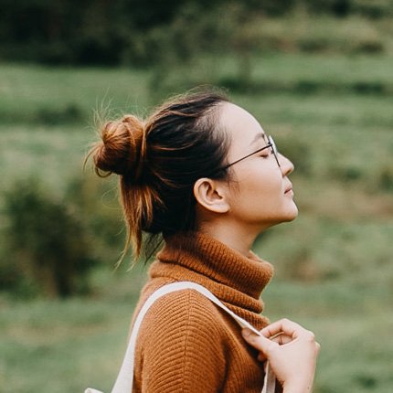 Side pic of woman with brown hair and glasses wearing rust coloured polo neck jumper